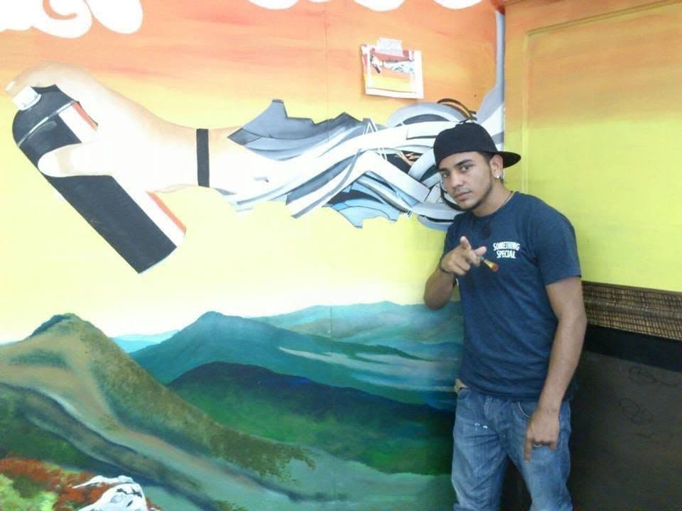 Alvir standing in front of a painted mural landscape.