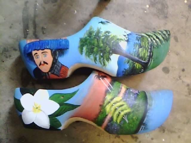 A pair of shoes hand-painted with a landscape and a flower.