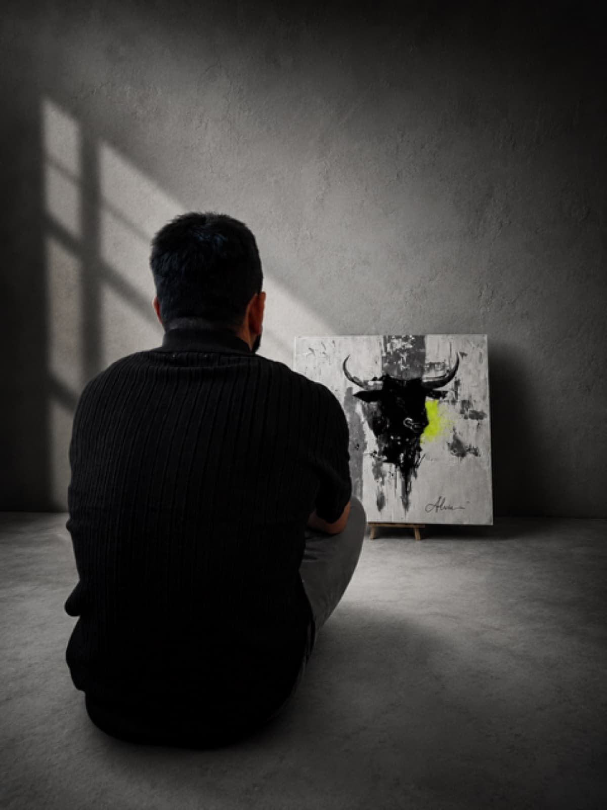 The artist sitting on the floor of an empty room, looking at the painting in window light