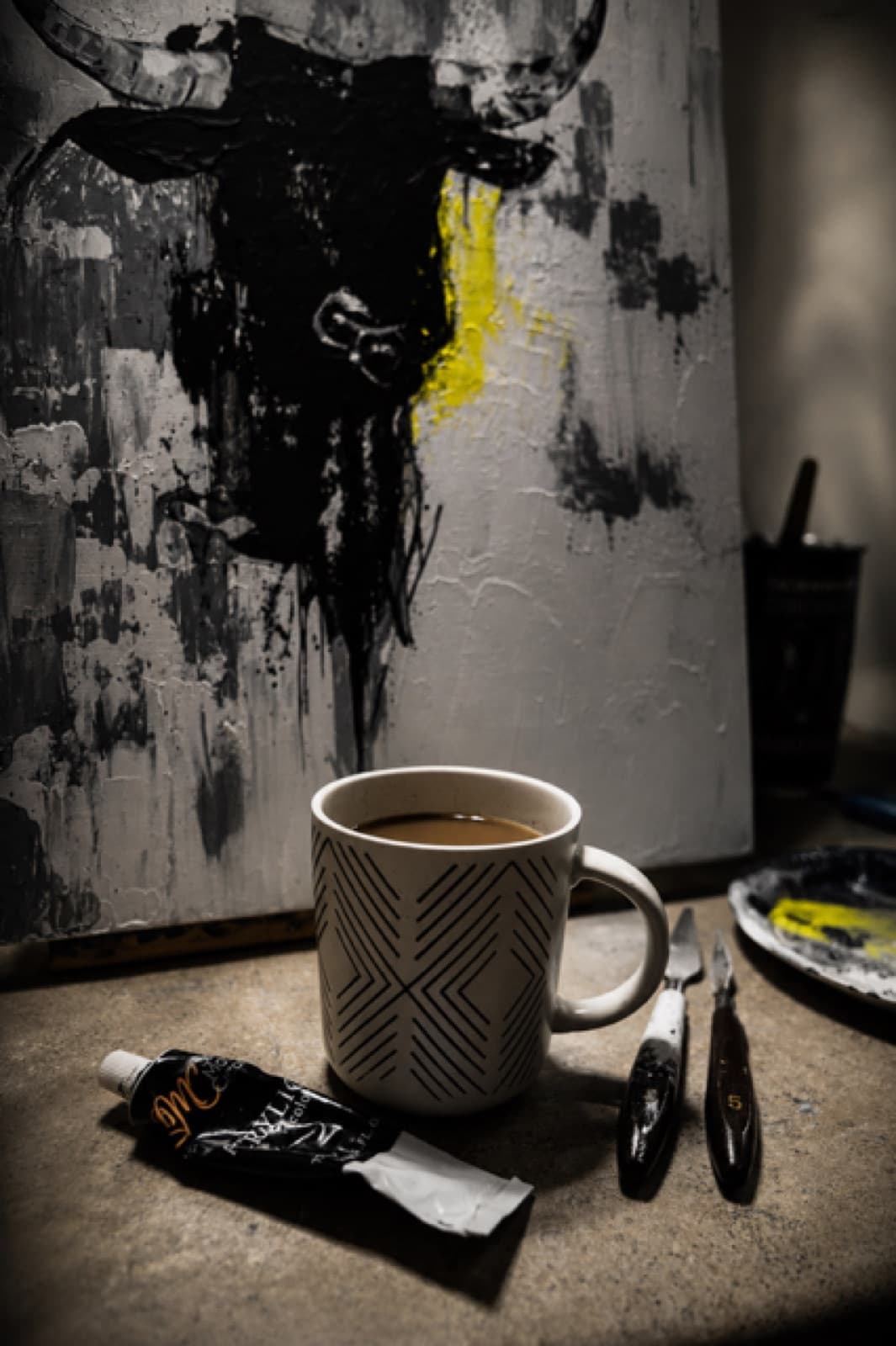 A mug of coffee, brushes and a squeezed tube of paint on the studio table, the canvas behind