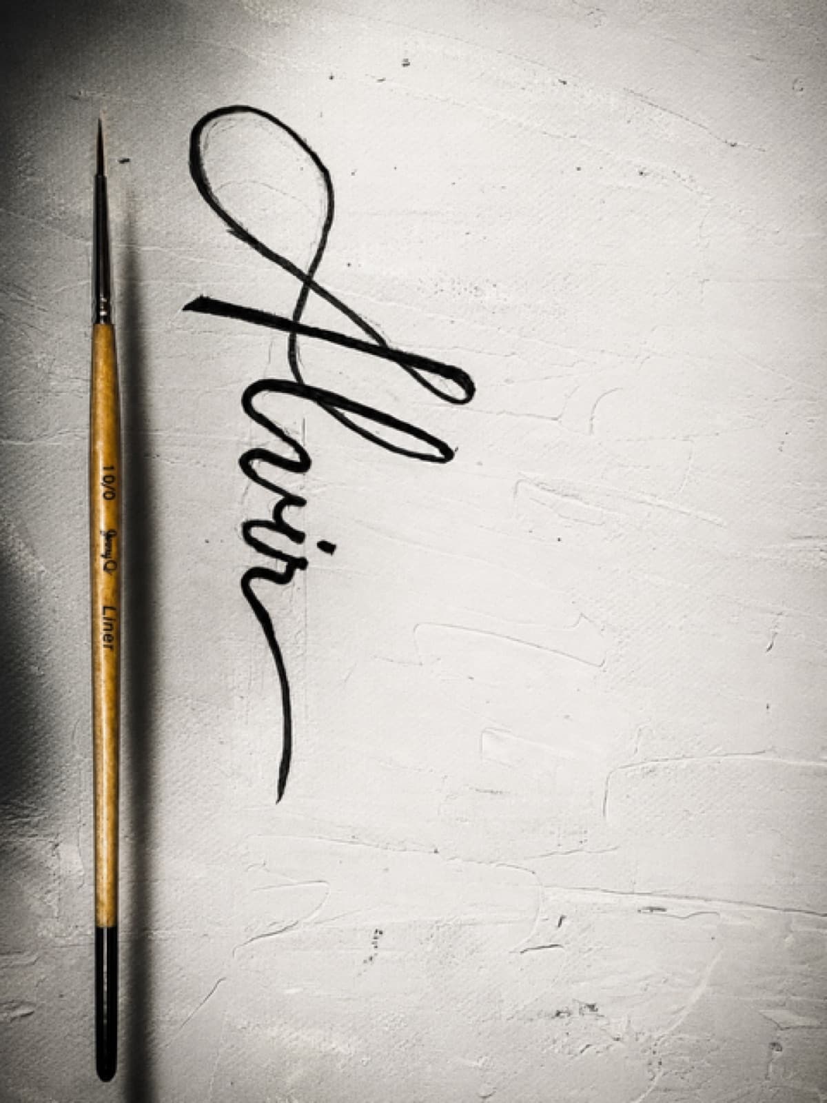 The signature drawn on raw canvas with a fine liner brush lying beside it
